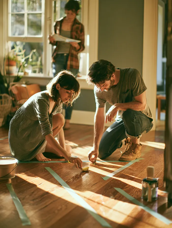 American couple marking wall measurements with painters tape in a new home